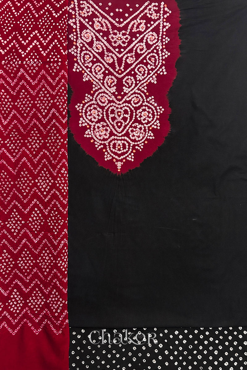 A black kurta set fabric with intricate bandhani & mirror embroidered contrast yoke, paired with a matching bottom & contrast red odhani placed on the left side featuring a zigzag design.