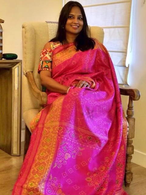 Chakor Patron in a pink patola saree sitting on a chair indoors.