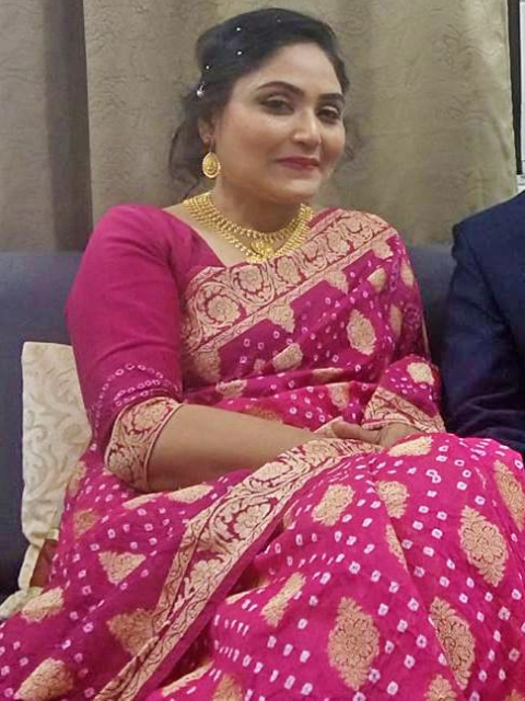 Chakor patron in a pink saree with gold patterns sitting on a couch.