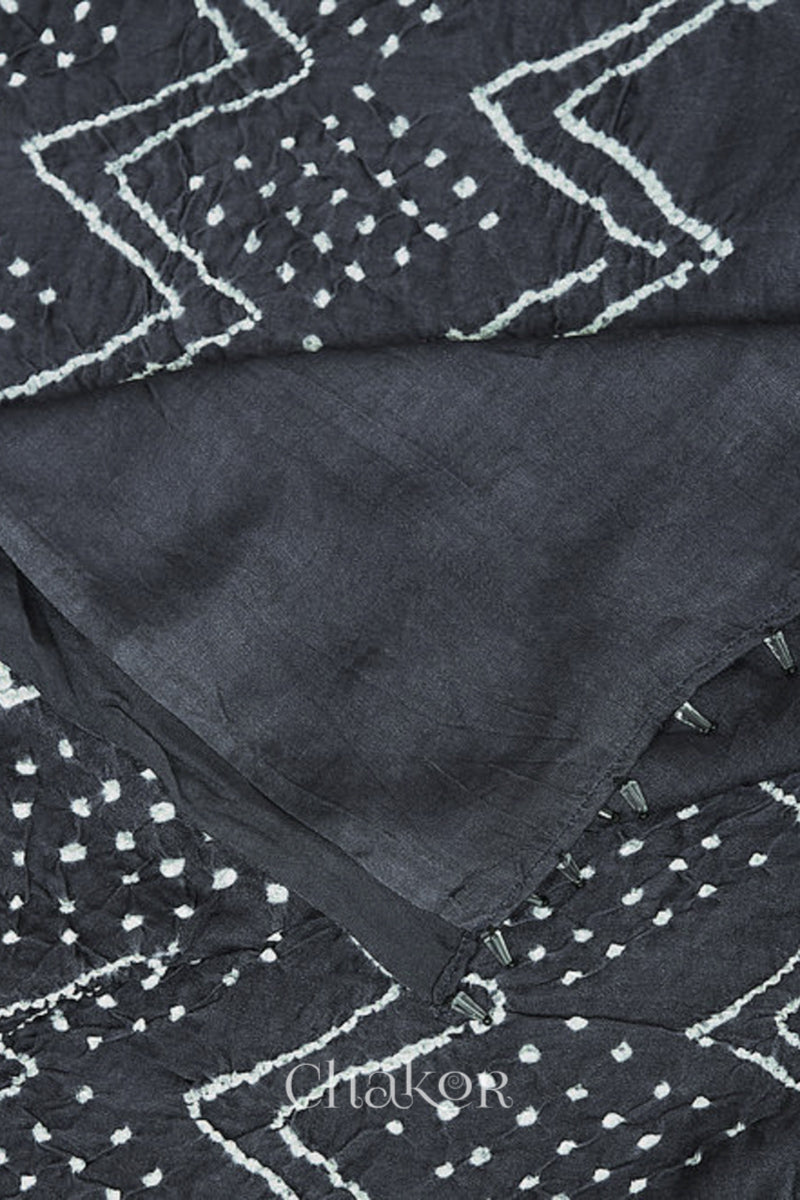 close-up of a charcoal grey rai bandhej dupatta in gaji silk,pallu edge detailed with beads.Text reads Chakor brand watermark.
