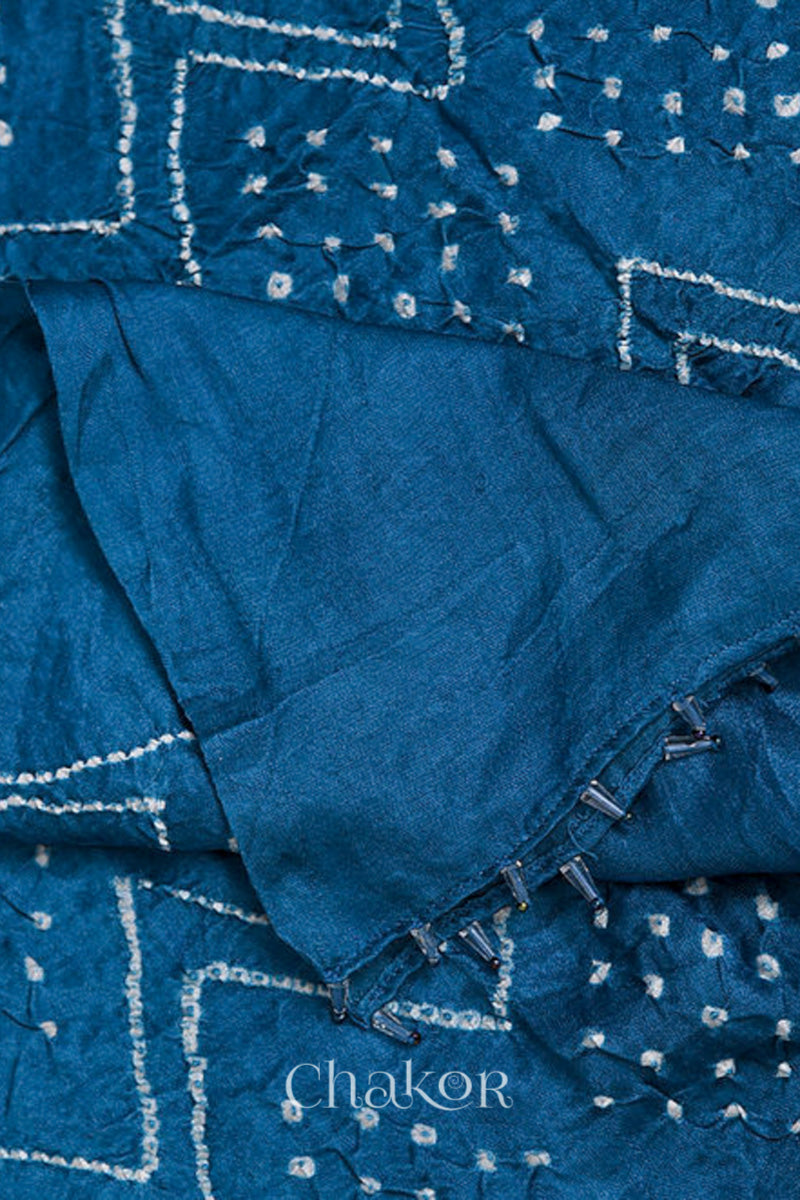 close-up of blue rai bandhej dupatta in gaji silk ,pallu edge detailed with beads.Text reads Chakor brand watermark.
