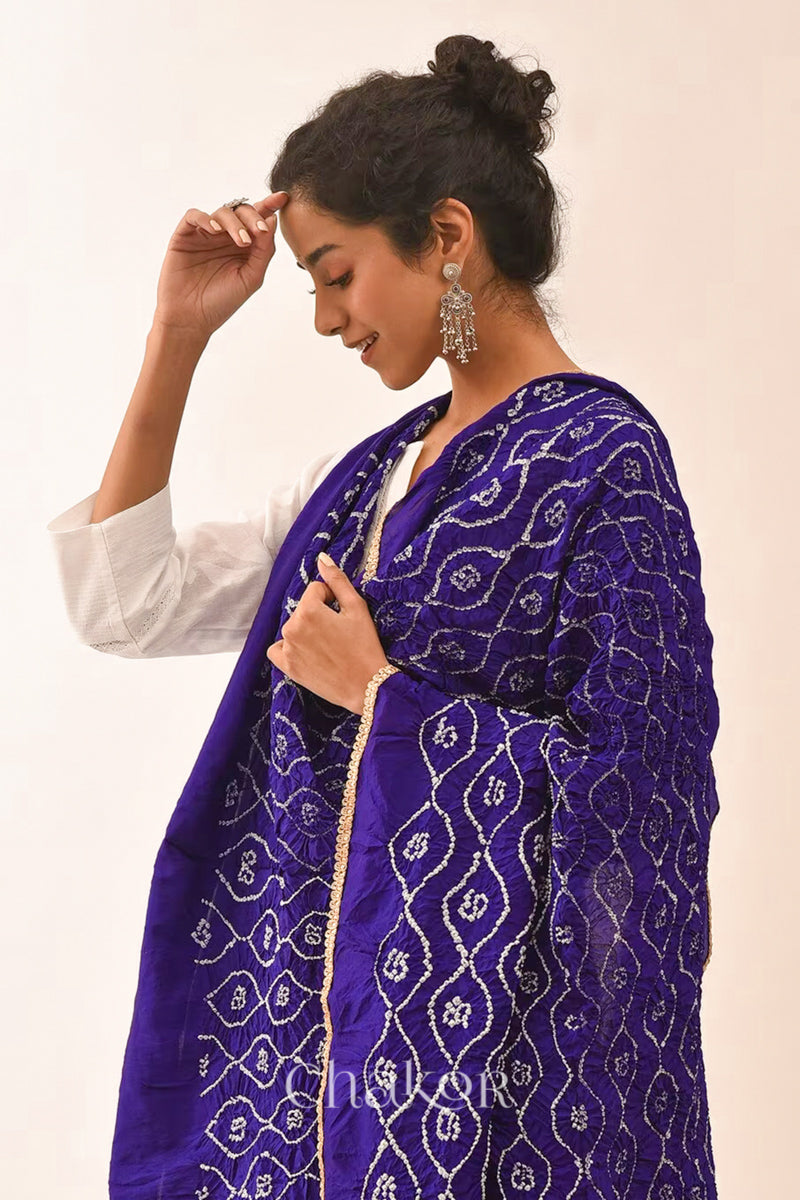 Woman wearing purple Bandhani mulberry silk dupatta with tie-dye dot pattern & detailed with golden lace.