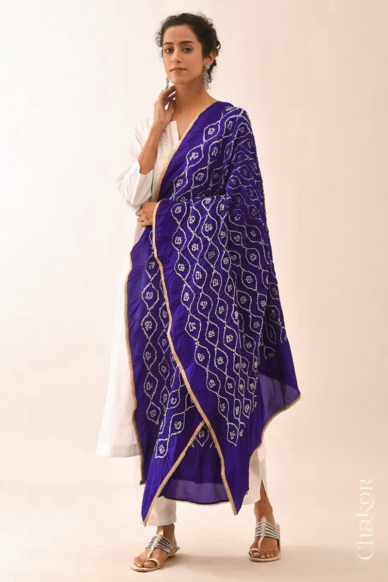 Woman wearing purple Bandhani mulberry silk dupatta with tie-dye dot pattern & detailed with golden lace.