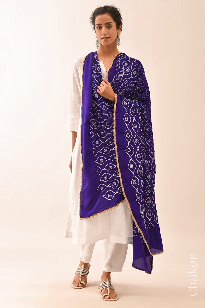 Woman wearing purple Bandhani mulberry silk dupatta with tie-dye dot pattern & detailed with golden lace.