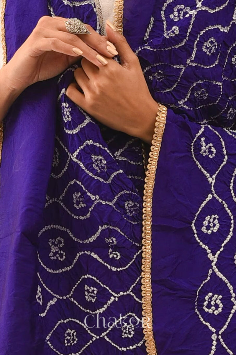 Close up of Woman wearing purple Bandhani mulberry silk dupatta with tie-dye dot pattern & detailed with golden lace.