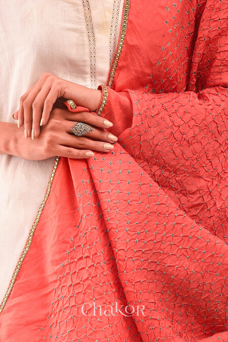 Close up of Woman wearing peach Bandhani mulberry silk dupatta with tie-dye dot pattern & detailed with golden lace.