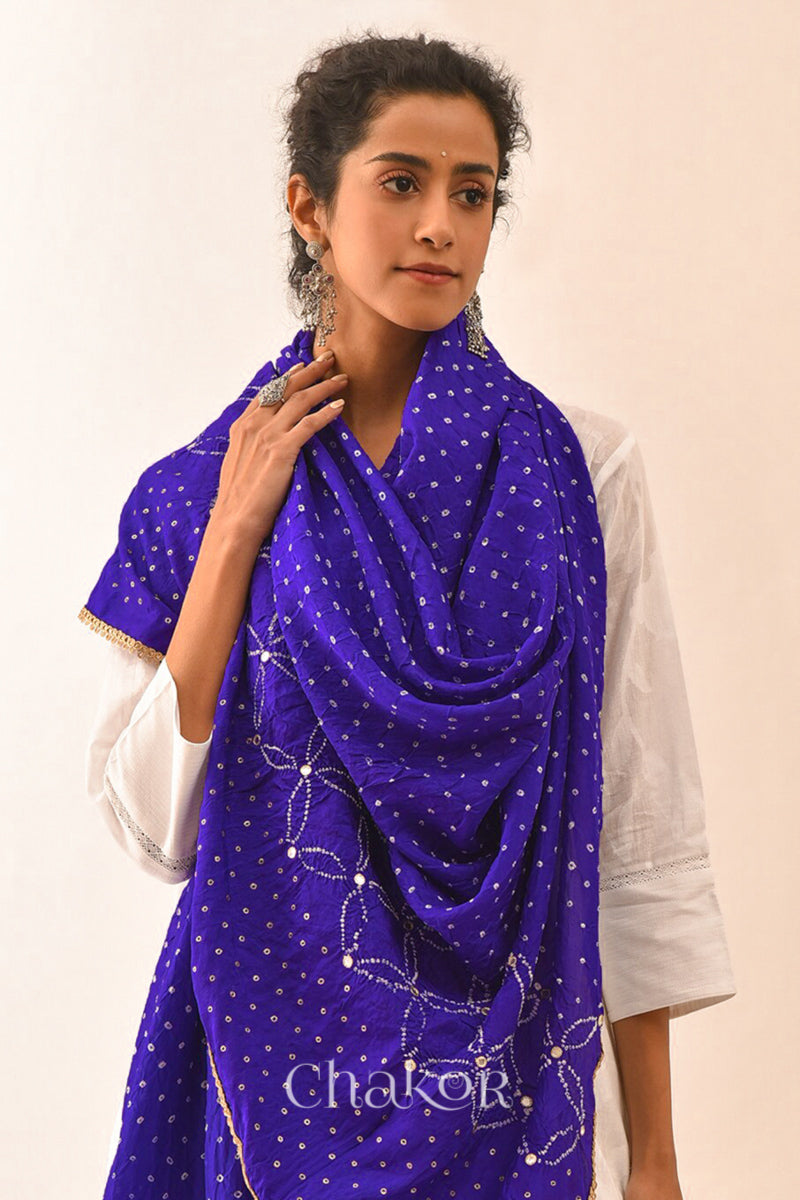 close-up of Women wearing purple Bandhani mulberry silk dupatta with tie-dye dot pattern & detailed with mirror work & golden lace on edge draped over a white kurta.
