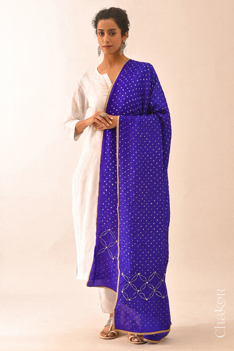 Women wearing purple Bandhani mulberry silk dupatta with tie-dye dot pattern & detailed with mirror work & golden lace on edge draped over a white kurta.