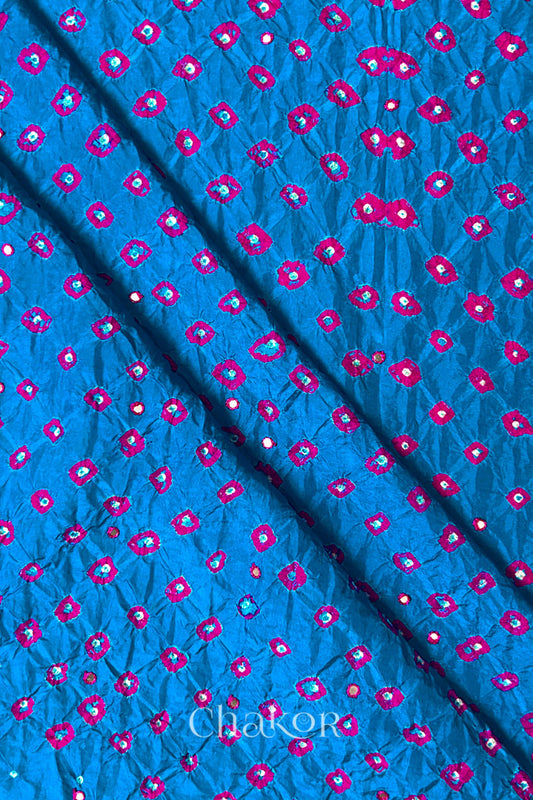 Close up of Peacock Blue Bandhani Mulberry Silk Fabric with pink bandhej dots and mirror embroidery.