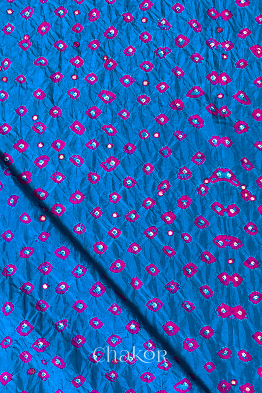 Close up of Peacock Blue Bandhani Mulberry Silk Fabric with pink bandhej dots and mirror embroidery.