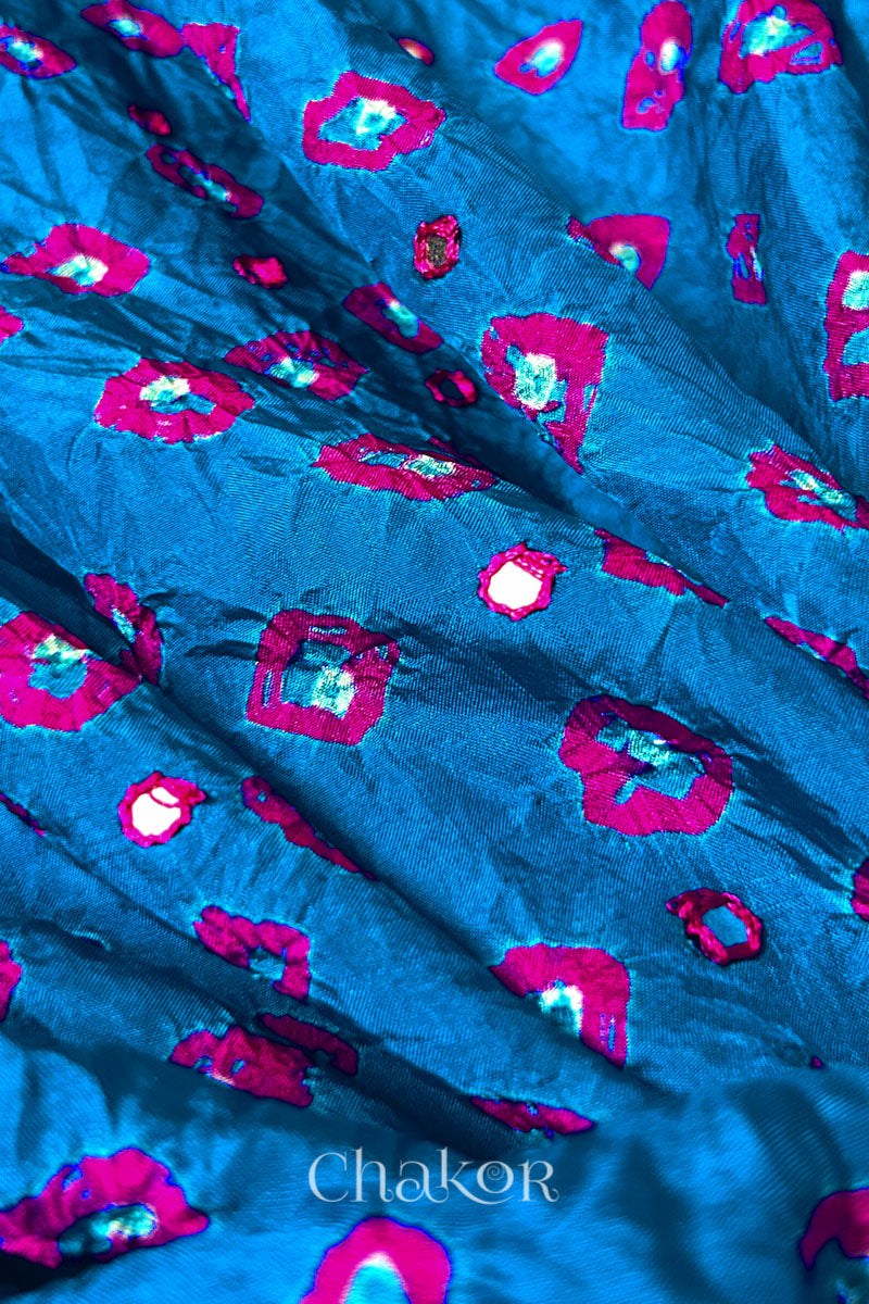 Close up of Peacock Blue Bandhani Mulberry Silk Fabric with pink bandhej dots and mirror embroidery.