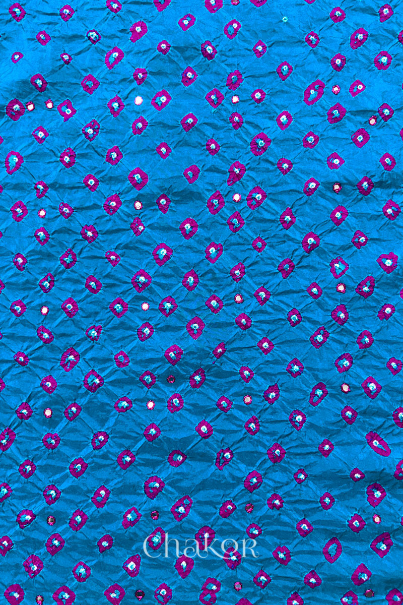 Close up of Peacock Blue Bandhani Mulberry Silk Fabric with pink bandhej dots and mirror embroidery.