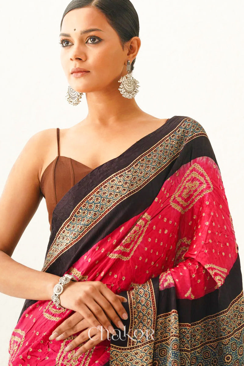 Woman wearing Coral Pink Bandhani Saree with Black Ajrakh printed border and pallu in pure gaji silk with traditional bandhej tie-dye, handcrafted in Kutch. 