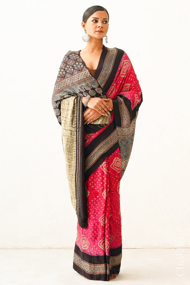Woman wearing Coral Pink Bandhani Saree with Black Ajrakh printed border and pallu in pure gaji silk with traditional bandhej tie-dye, handcrafted in Kutch. 