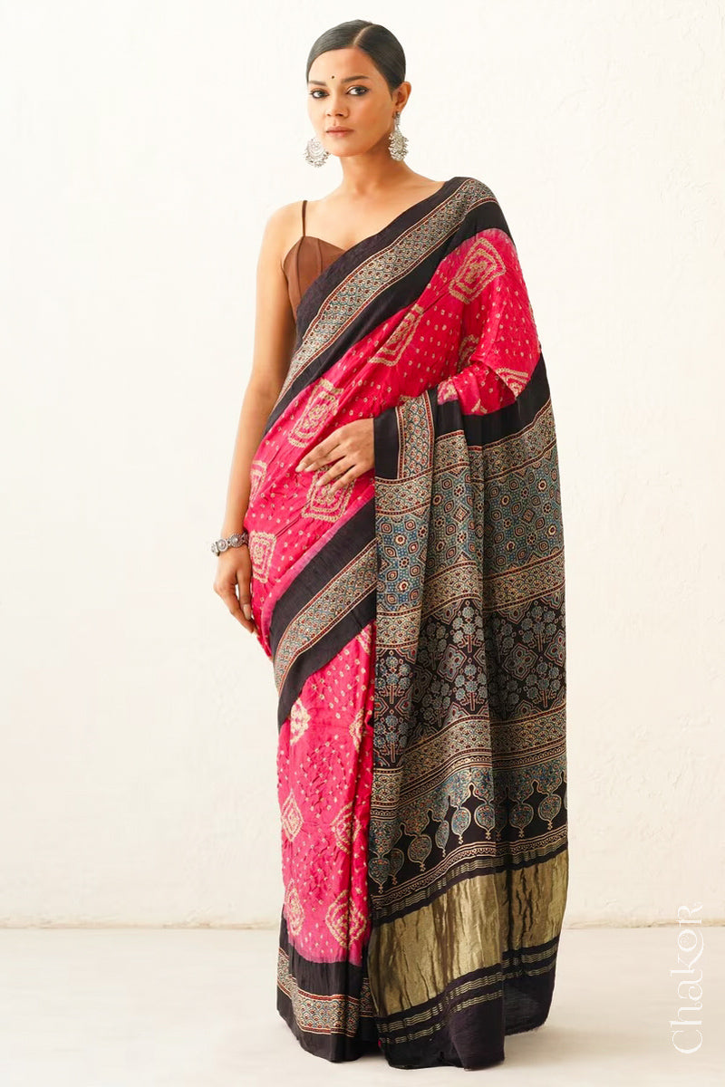 Woman wearing Coral Pink Bandhani Saree with Black Ajrakh printed border and pallu in pure gaji silk with traditional bandhej tie-dye, handcrafted in Kutch. 