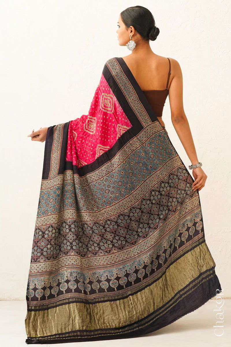 Woman wearing Coral Pink Bandhani Saree with Black Ajrakh printed border and pallu in pure gaji silk with traditional bandhej tie-dye, handcrafted in Kutch. 