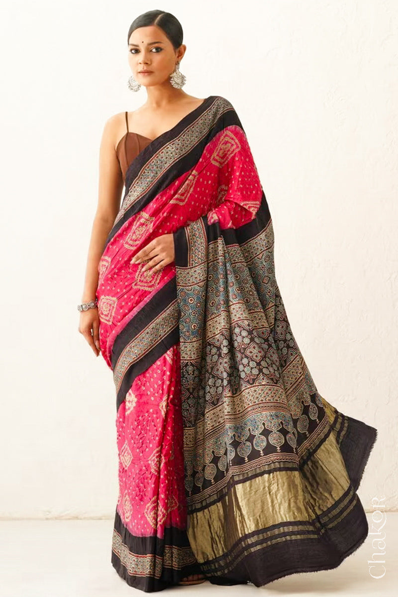 Woman wearing Coral Pink Bandhani Saree with Black Ajrakh printed border and pallu in pure gaji silk with traditional bandhej tie-dye, handcrafted in Kutch. 