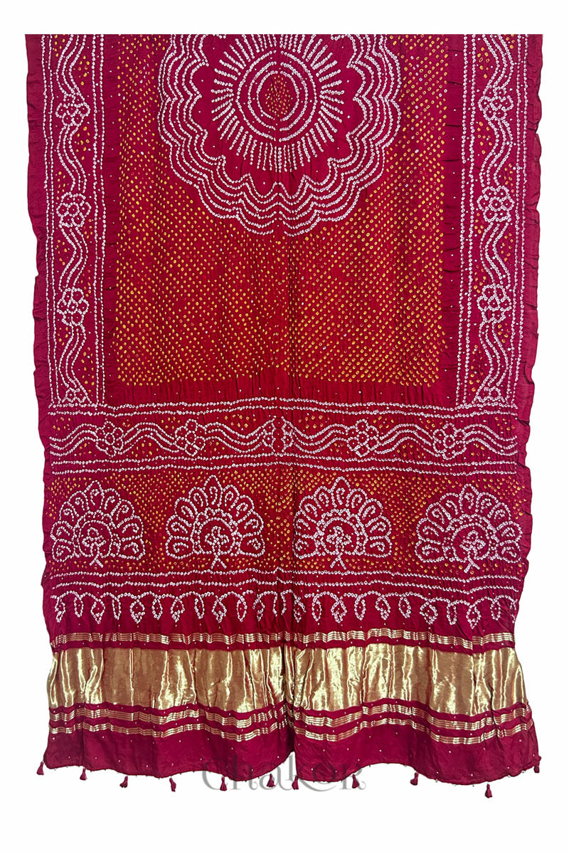 A vibrant red dupatta showcasing intricate rai bandhej in red & yellow with a shimmering gold band on the pallu and tassels on the hem. Text reads Chakor brand watermark.

