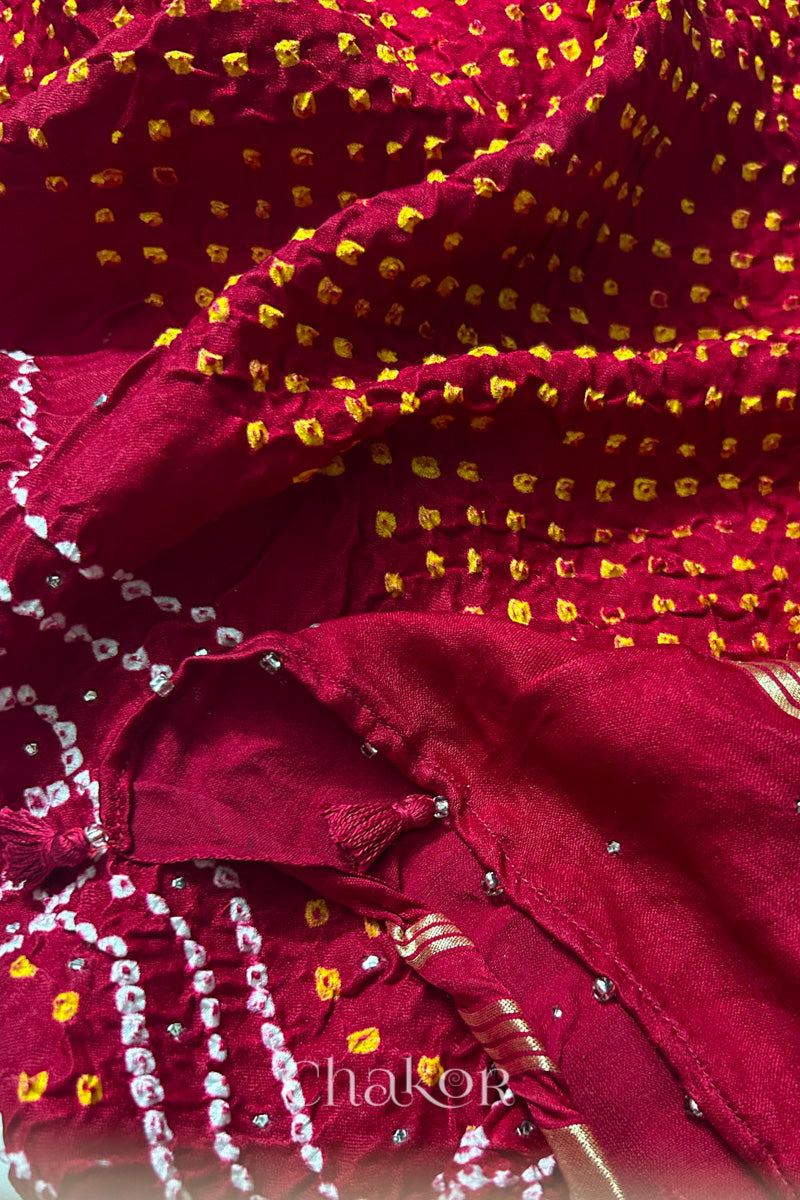 Close-up of a rai bandhej dupatta in red featuring white & yellow bandhani dots along with tassels.Text reads Chakor brand watermark.