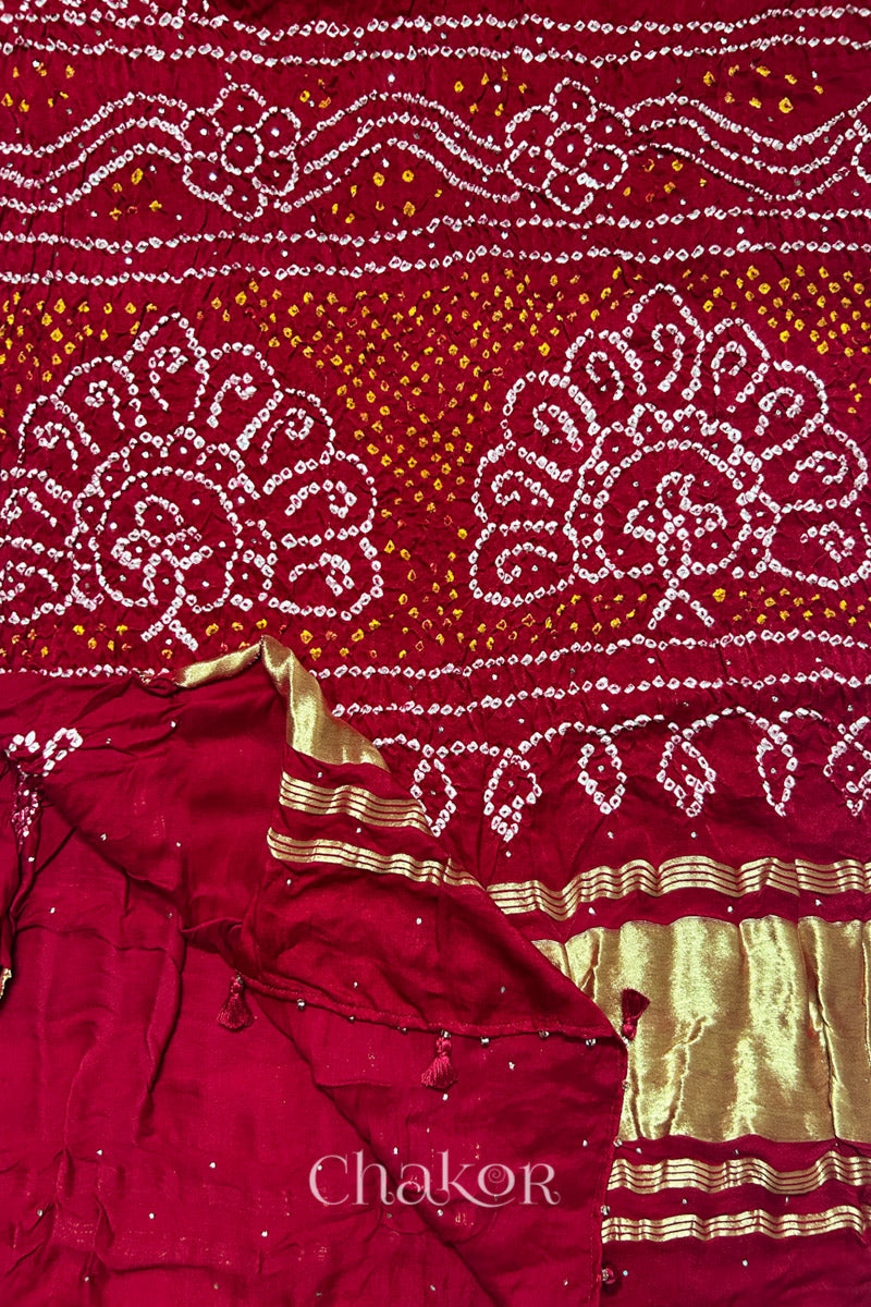Red gaji silk dupatta showcasing rai bandhej accented with mukaish work with tissue band folded on corner. 