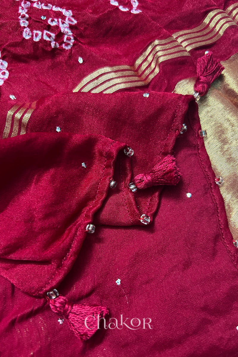 Close-up of a rai bandhej dupatta in red featuring tassel detail on the folded hem.Text reads Chakor brand watermark.
