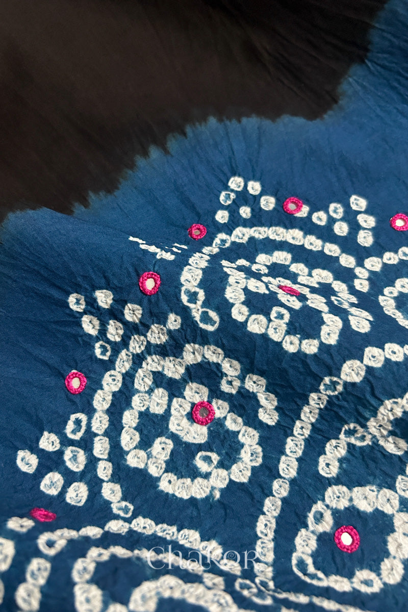Close-up of  black fabric adorned with intricate traditional bandhani patterns and mirror embroidery on indigo blue yoke, showcasing beautiful craftsmanship.
