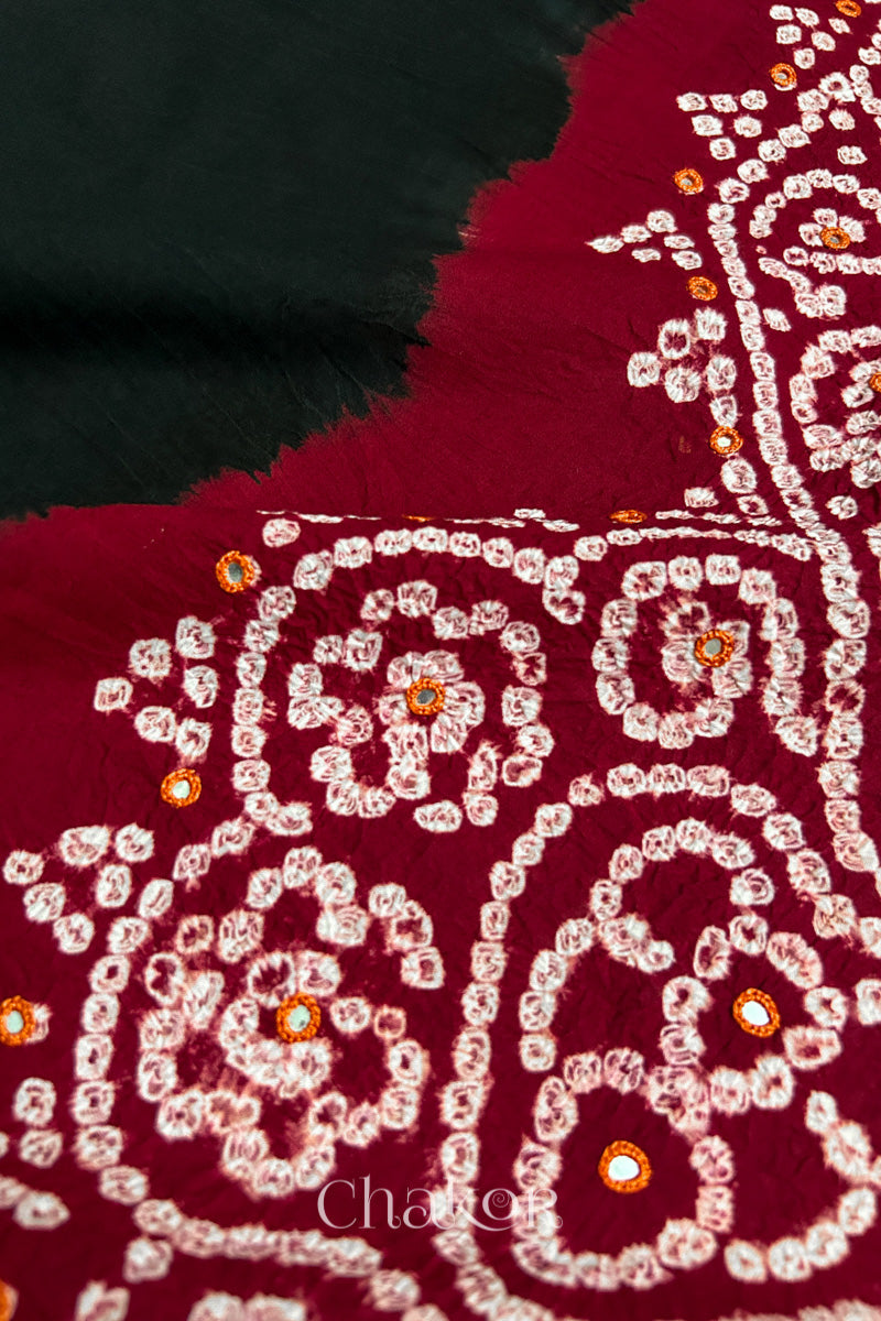 Close-up of  black fabric adorned with intricate traditional bandhani patterns and mirror embroidery on red yoke, showcasing beautiful craftsmanship.