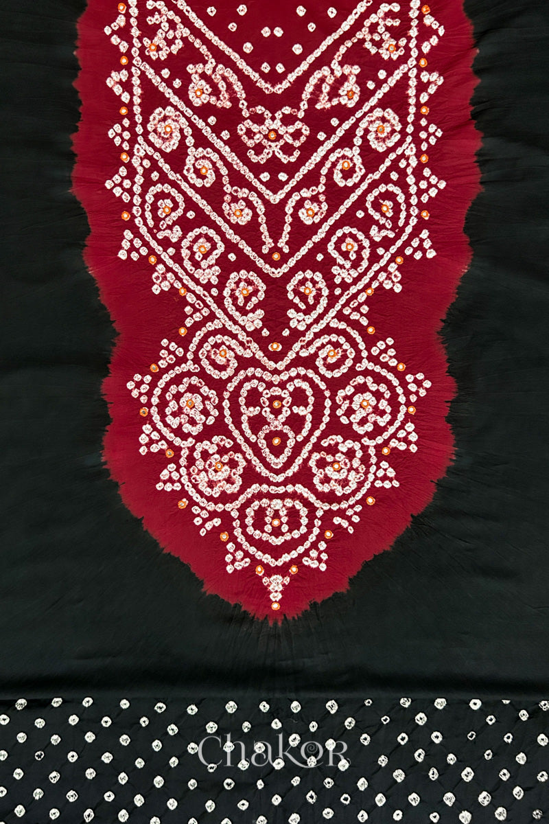 Close-up of tie dyed black kurta fabric featuring intricate bandhani and embroidered on contrasting red yoke with matching bandhani dotted bottom fabric, with Chakor brand logo.
