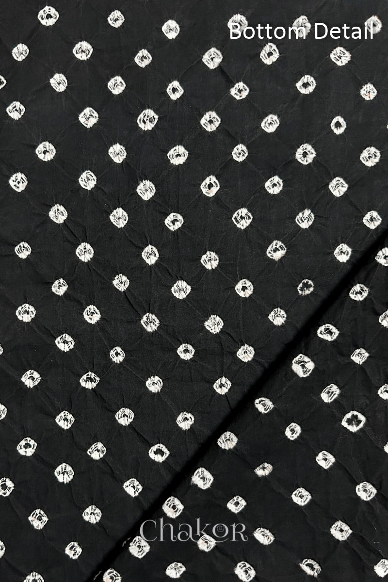 Close up of bottom fabric in  black patterned with bandhani tie dye dots, folded at the corner displaying texture and detail. Text reads bottom.
