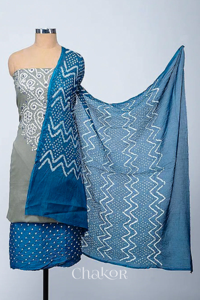 A stylish kurta set fabric featuring a cement grey mirror embroidered indigo blue top, a bandhani indigo blue bottom, and a matching indigo blue dupatta draped elegantly. Text reads Chakor.
