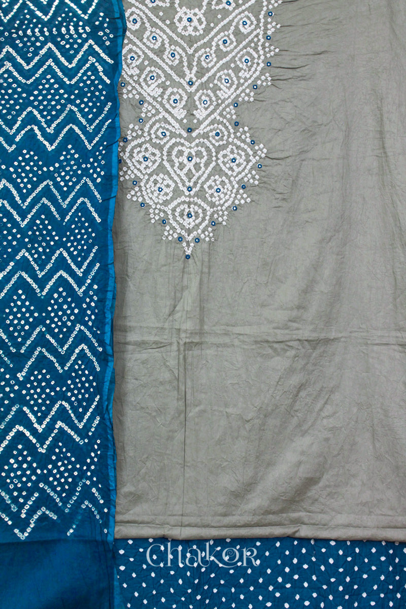 A cement grey kurta set fabric with intricate white bandhani & mirror embroidery, paiindigo blue with a indigo blue bottom & odhani featuring a zigzag design.
