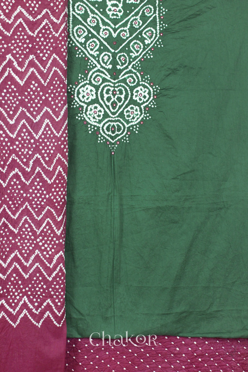 A moss green kurta set fabric with intricate white bandhani & mirror embroidery, paiplum pink with a plum pink bottom & odhani featuring a zigzag design.
