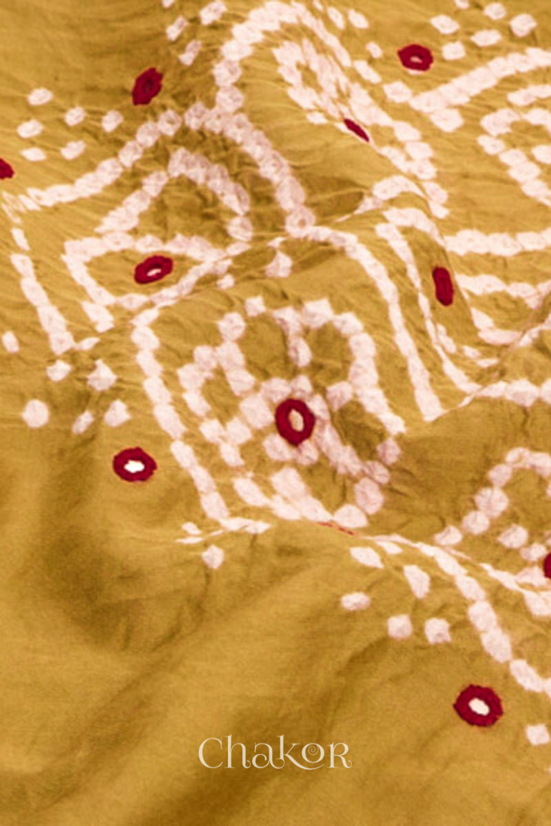 Close-up of bandhani yoke kurta fabric featuring intricate tie-dye and red embroidered patterns on an mustard background, with Chakor brand logo.
