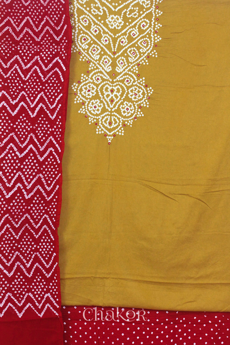 A mustard kurta set fabric with intricate white bandhani & mirror embroidery, paired with a red bottom & odhani featuring a zigzag design.

