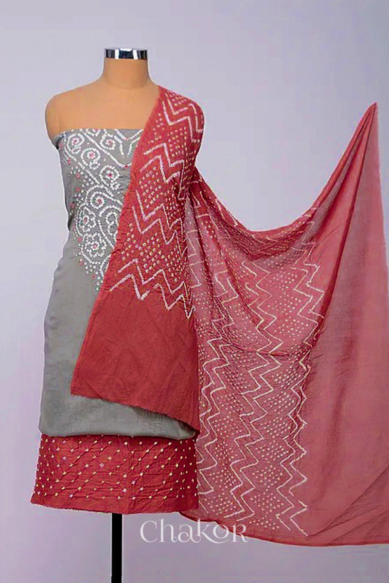 A stylish kurta set fabric featuring a grey mirror embroidered top, a bandhani dusty red bottom, and a matching dusty red dupatta draped elegantly. Text reads Chakor.
