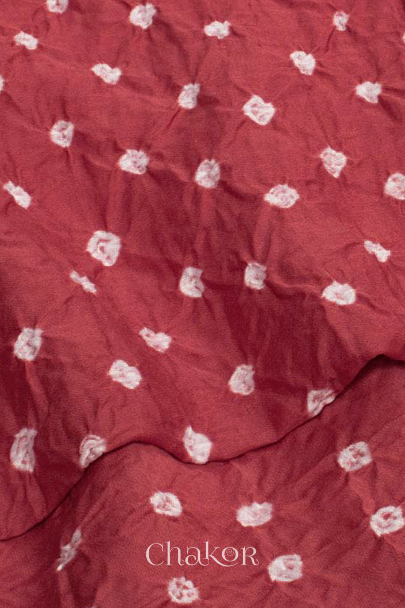 Close up of Bottom fabric in dusty red patterned with simple bandhani tie dye dots, draped neatly on a dress form, with Chakor brand logo.
