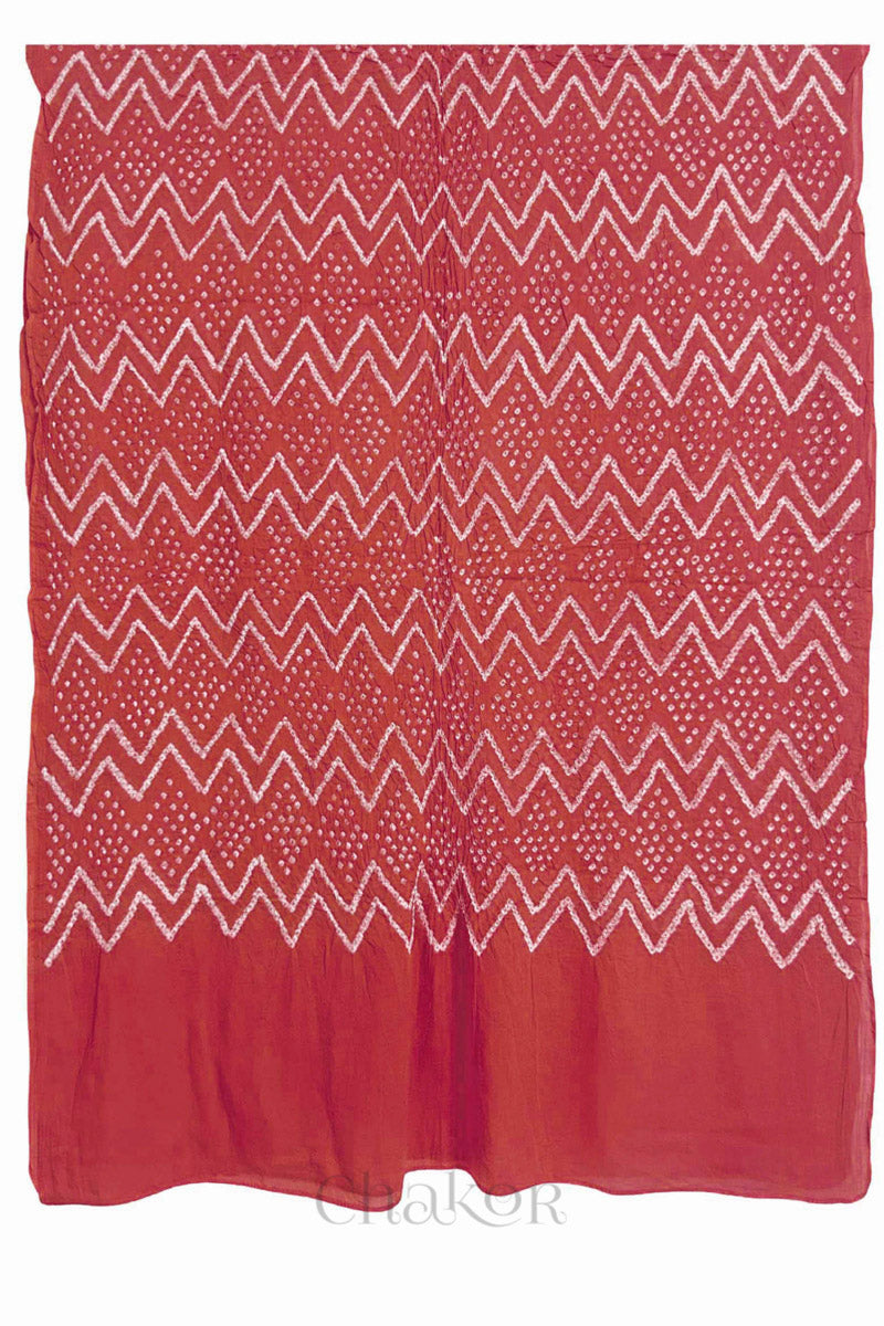 A dusty red cotton mul dupatta featuring intricate white zigzag bandhani dot patterns, showcasing traditional design.
