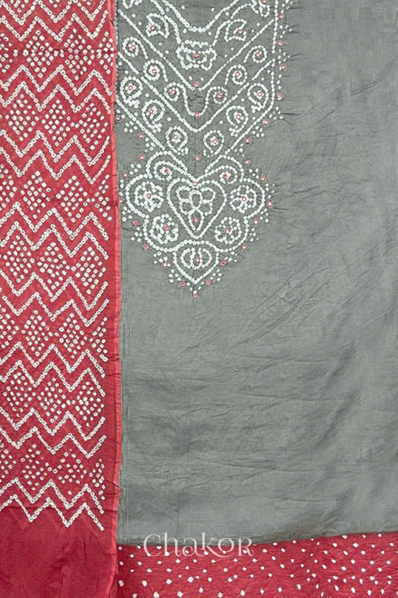 A grey kurta set fabric with intricate white bandhani & mirror embroidery, paired with a dusty red bottom & odhani featuring a zigzag design.
