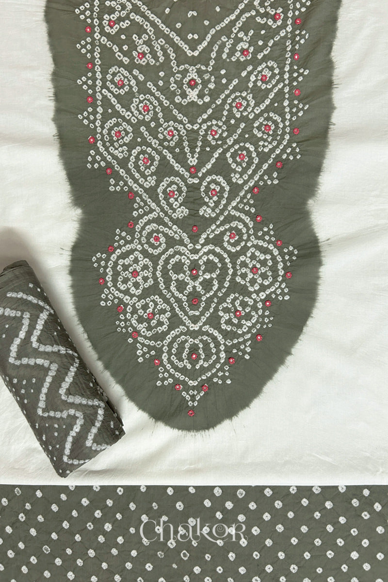 A stylish set fabric featuring a grey mirror embroidered yoke on a white kurta, bandhani grey bottom and dupatta rolled beautifully and placed on the fabric. Text reads Chakor.