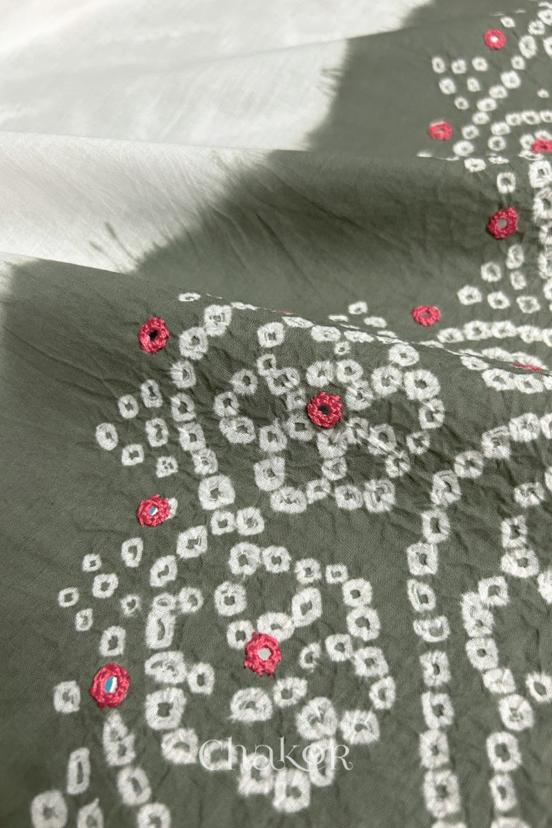 Close-up of grey-white fabric adorned with intricate traditional bandhani patterns and pink mirror embroidery, showcasing beautiful craftsmanship.