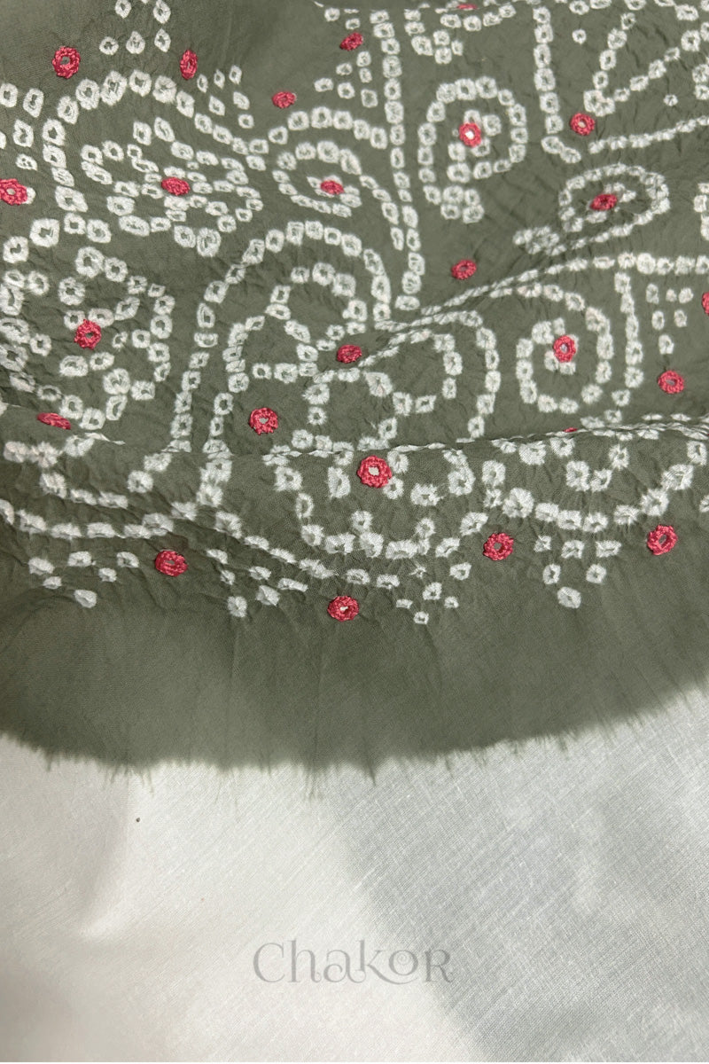 Close-up of grey-white fabric adorned with intricate traditional bandhani patterns and pink mirror embroidery, showcasing beautiful craftsmanship.
