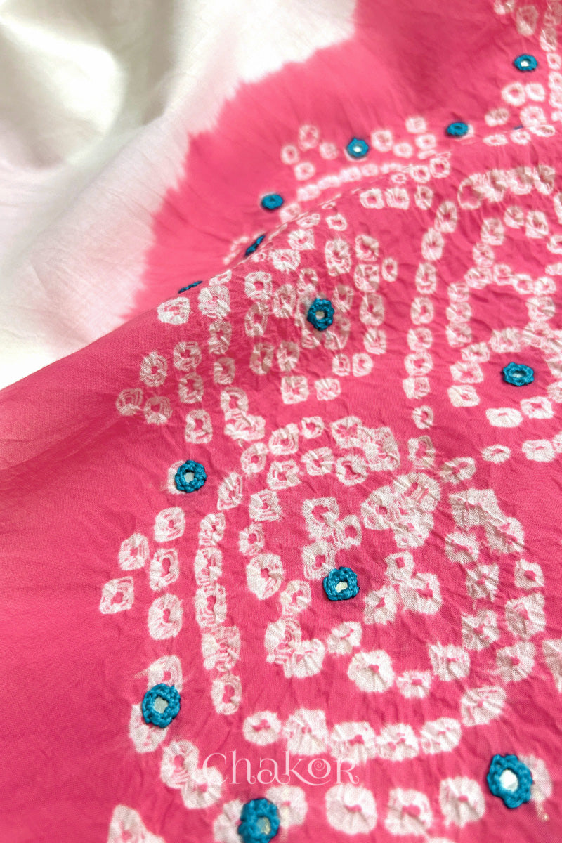 Close-up of pink-white fabric adorned with intricate traditional bandhani patterns and blue mirror embroidery, showcasing beautiful craftsmanship.