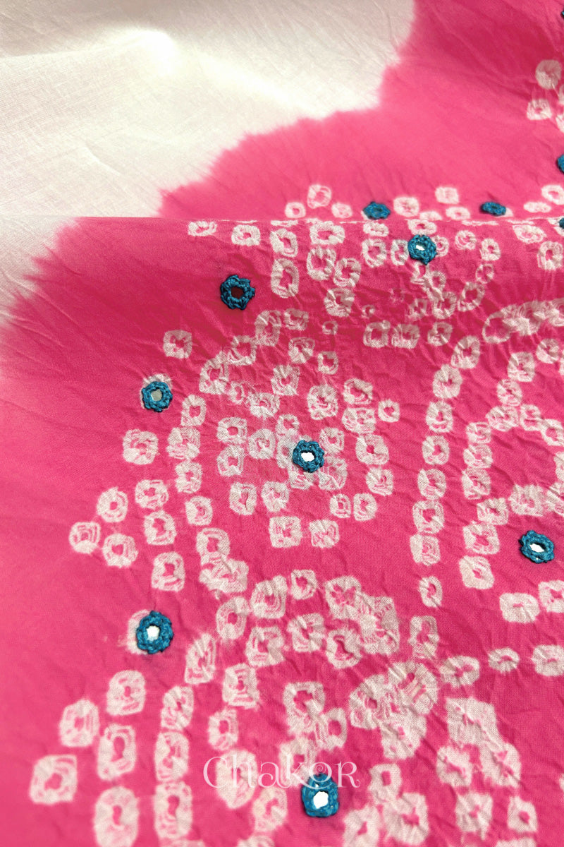 Close-up of pink-white fabric adorned with intricate traditional bandhani patterns and blue mirror embroidery, showcasing beautiful craftsmanship.