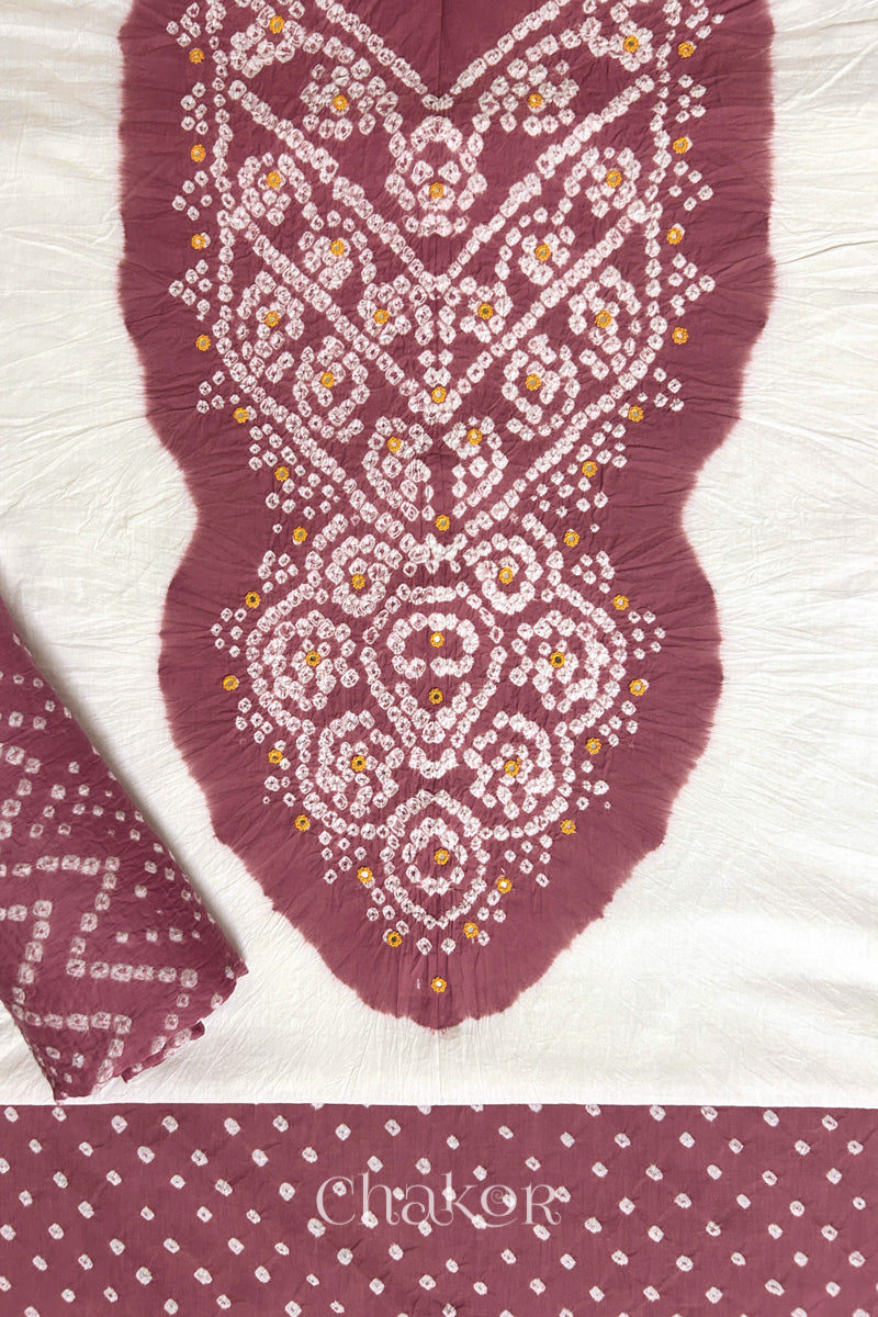 A stylish set fabric featuring a soft rose pink mirror embroidered yoke on a white kurta, bandhani soft rose pink bottom and dupatta rolled beautifully and placed on the fabric. Text reads Chakor.