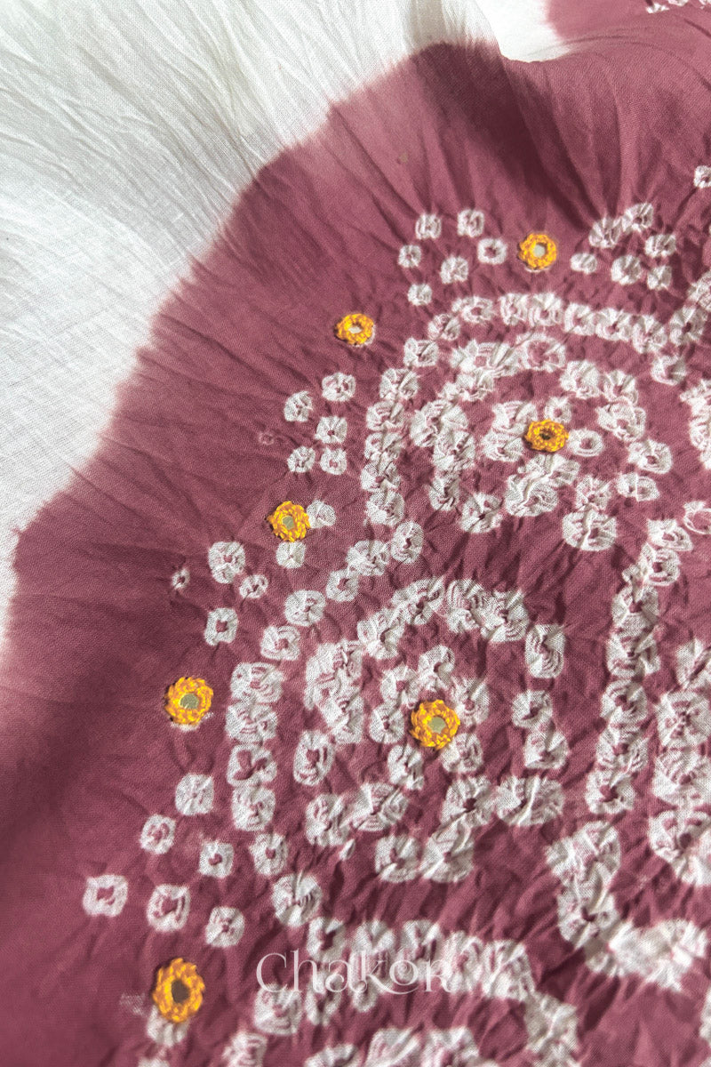 Close-up of soft rose pink-white fabric adorned with intricate traditional bandhani patterns and yellow mirror embroidery, showcasing beautiful craftsmanship.