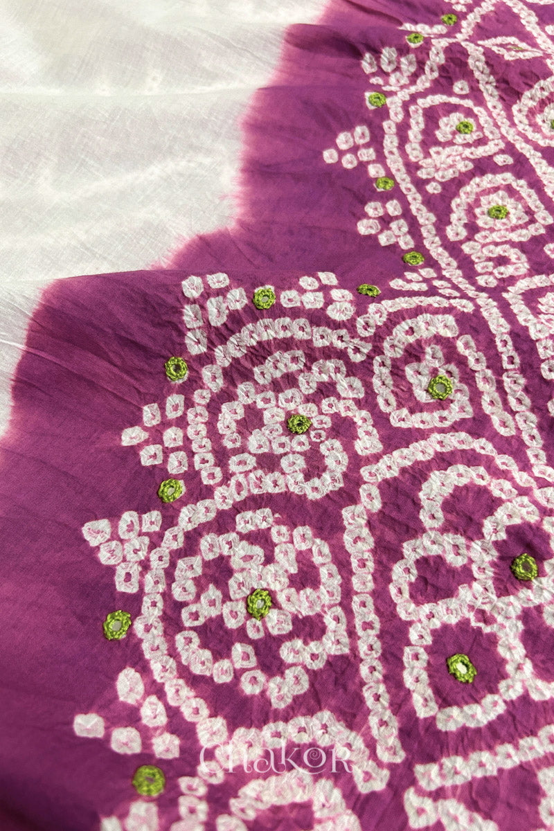 Close-up of deep violet-white fabric adorned with intricate traditional bandhani patterns and parrot green mirror embroidery, showcasing beautiful craftsmanship.