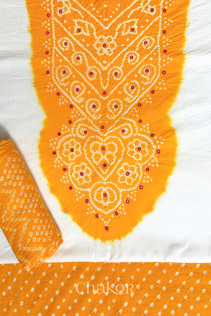A stylish set fabric featuring a yellow mirror embroidered yoke on a white kurta, bandhani yellow bottom and dupatta rolled beautifully and placed on the fabric. Text reads Chakor.