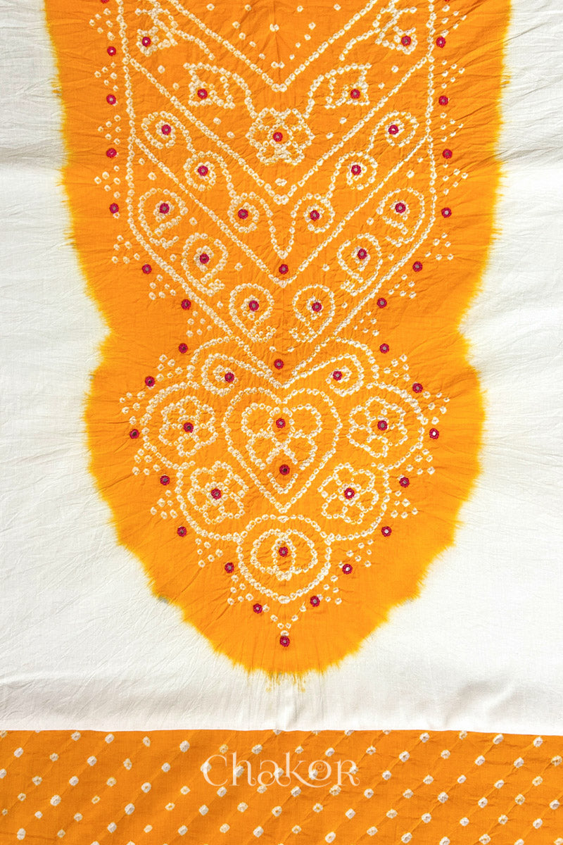 Close-up of tie dyed yellow yoke on white kurta fabric featuring intricate bandhani and embroidered patterns with yellow bandhani dotted bottom fabric, with Chakor brand logo.