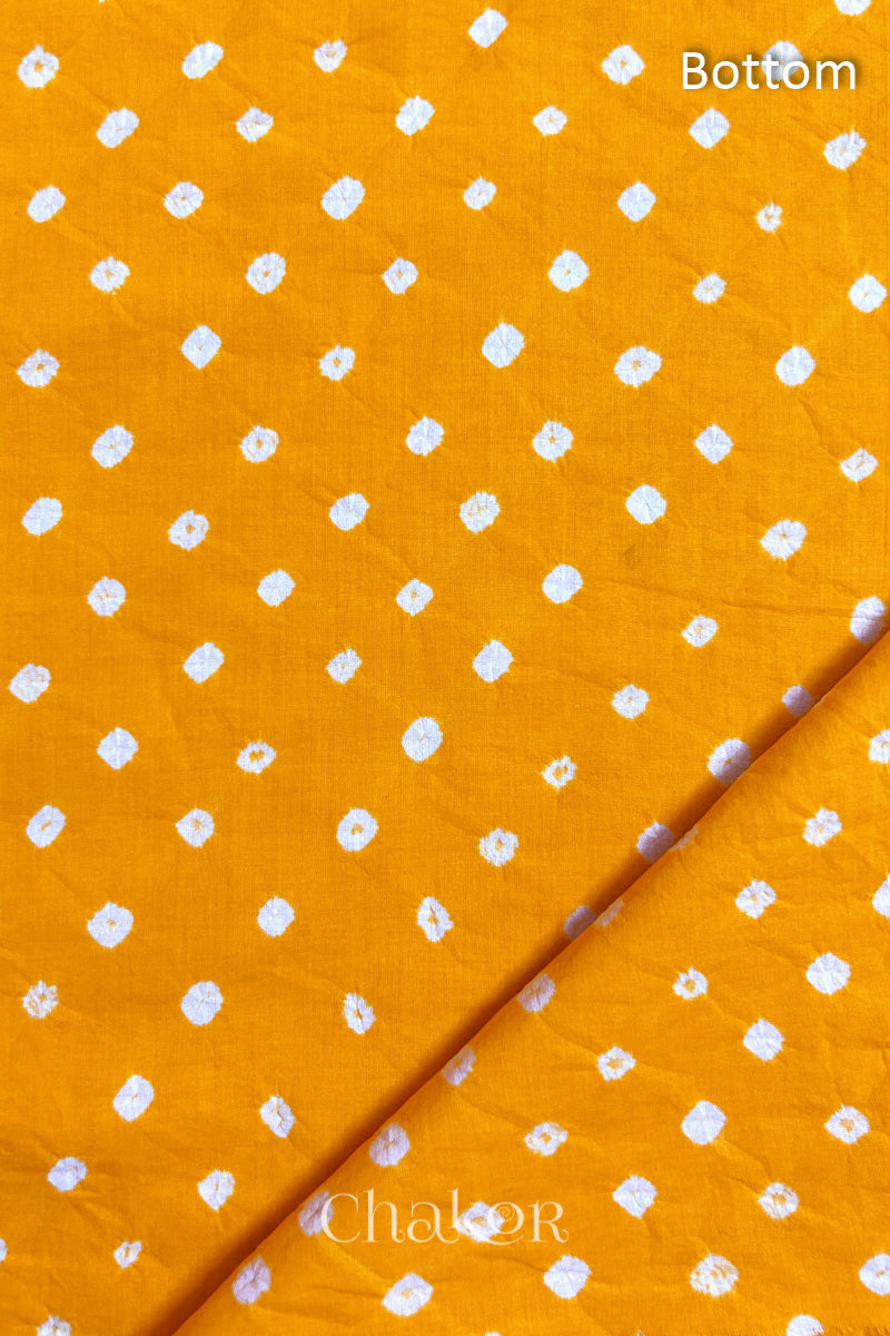 Close up of Bottom fabric in yellow patterned with bandhani tie dye dots, folded at the corner displaying texture and detail.