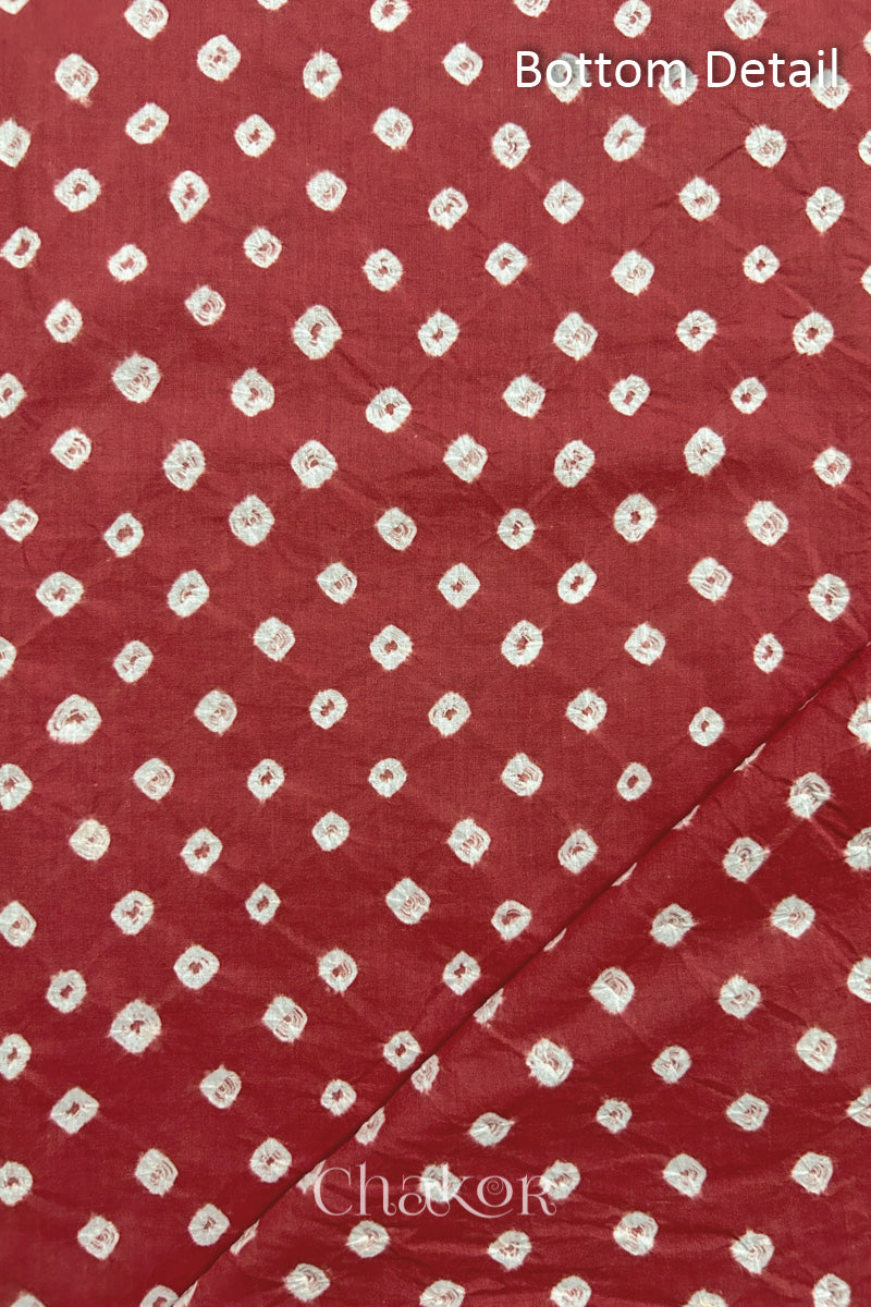 Close up of bottom fabric in  brick red patterned with bandhani tie dye dots, folded at the corner displaying texture and detail. Text reads bottom.